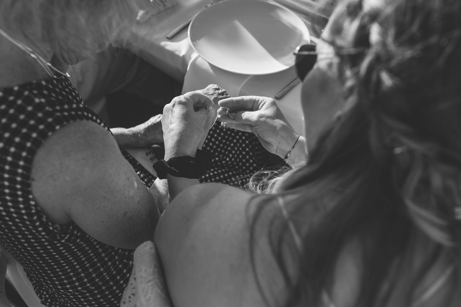 Black and white over-shoulder image of Santorini wedding guest helps other guest put on a bracelet.