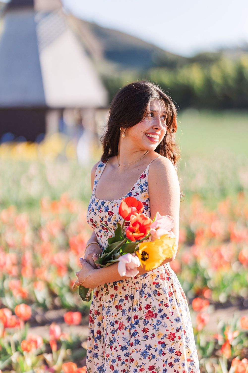Someone in a floral dress picks flowers in a colorful garden field on a bright sunny summer day.