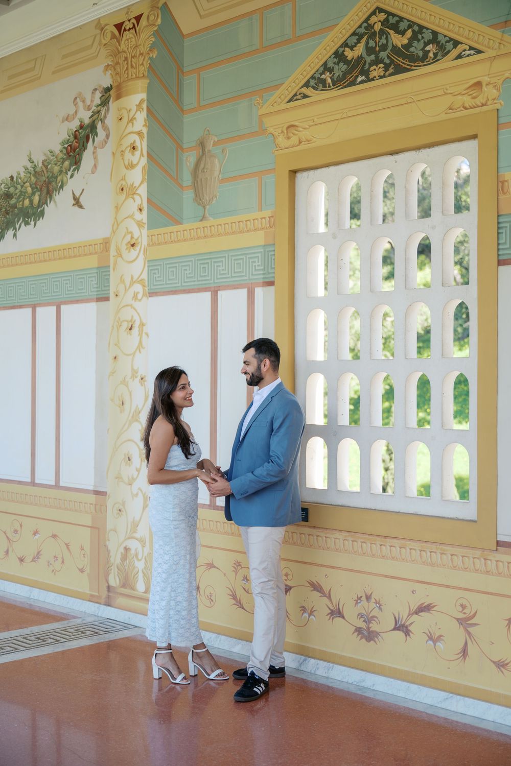 A couple shares a romantic moment in an elegant yellow and mint green veranda with ornate architectural details.