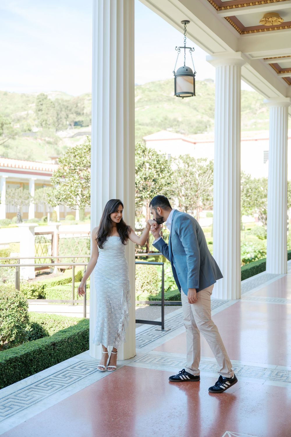 A romantic couple shares tender moments on an elegant white columned porch overlooking scenic hillside views.