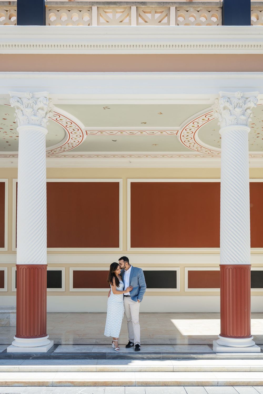 Architectural details of a classical colonnade with white columns and terracotta walls in a symmetrical composition.