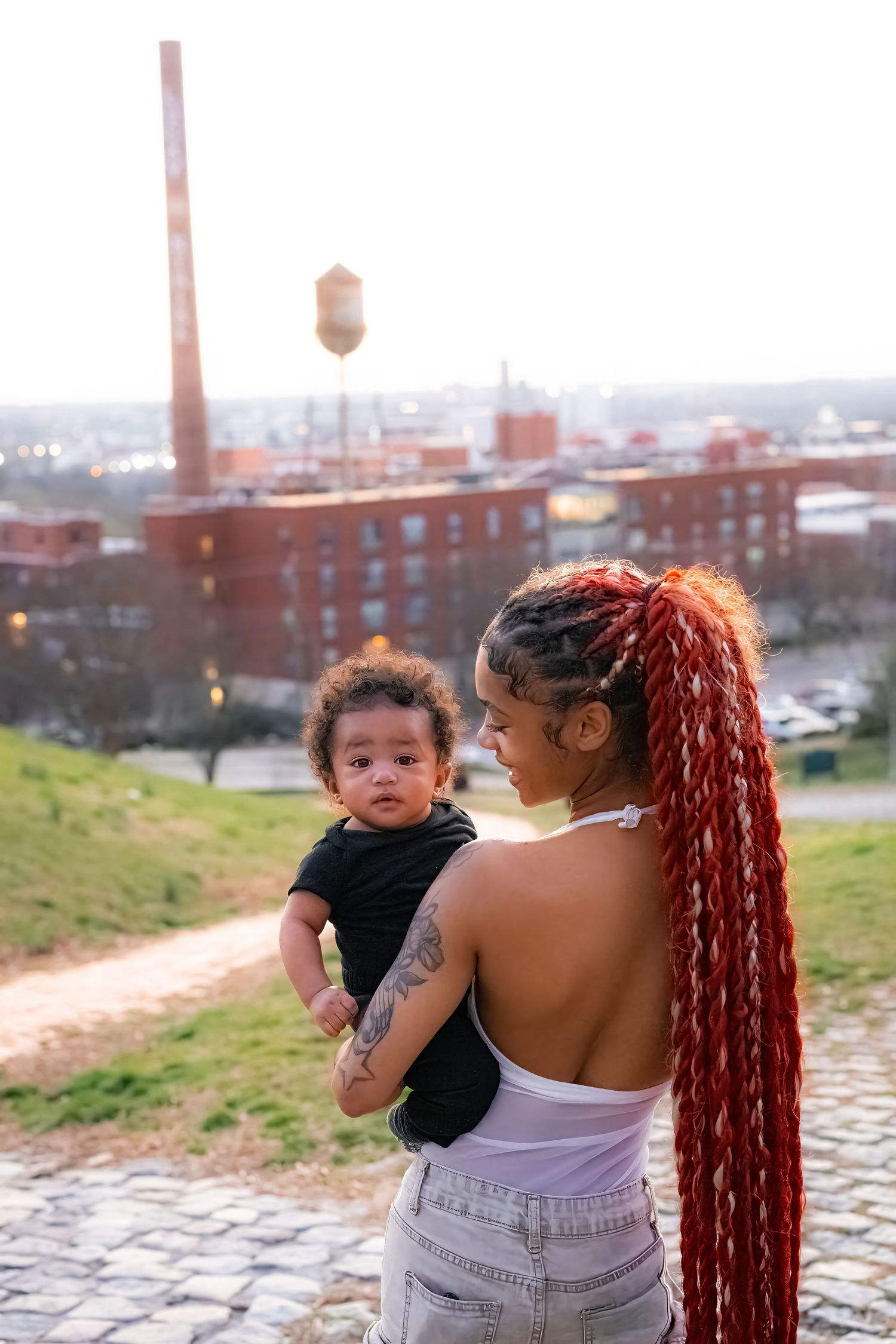 Parent and child share a tender moment outdoors against an urban industrial backdrop.