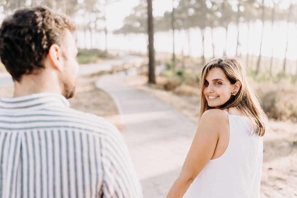 A couple in casual attire shares intimate moments while walking along a scenic coastal path during sunset.