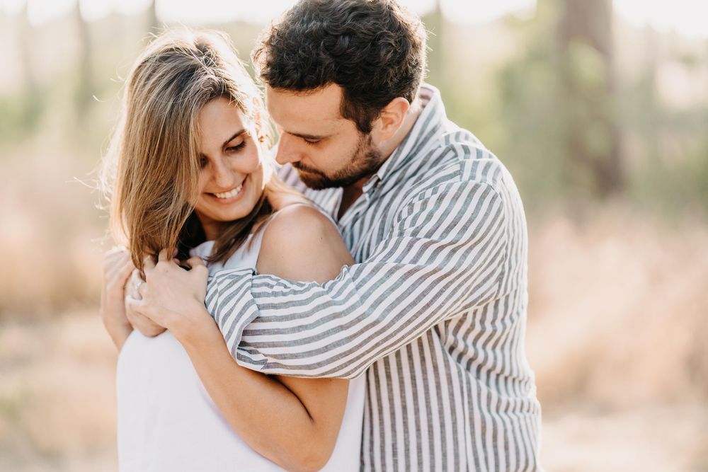 A couple shares tender moments in an outdoor setting wearing neutral tones and stripes.