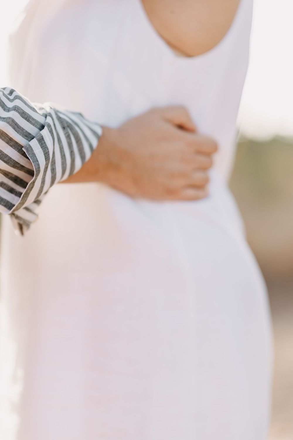 Close-up view of a pregnant person's belly in a white dress with striped sleeves showing during maternity photoshoot.