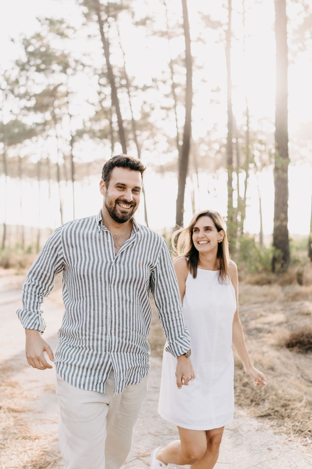 A couple walks together on a forest path in soft lighting, wearing casual summer outfits.