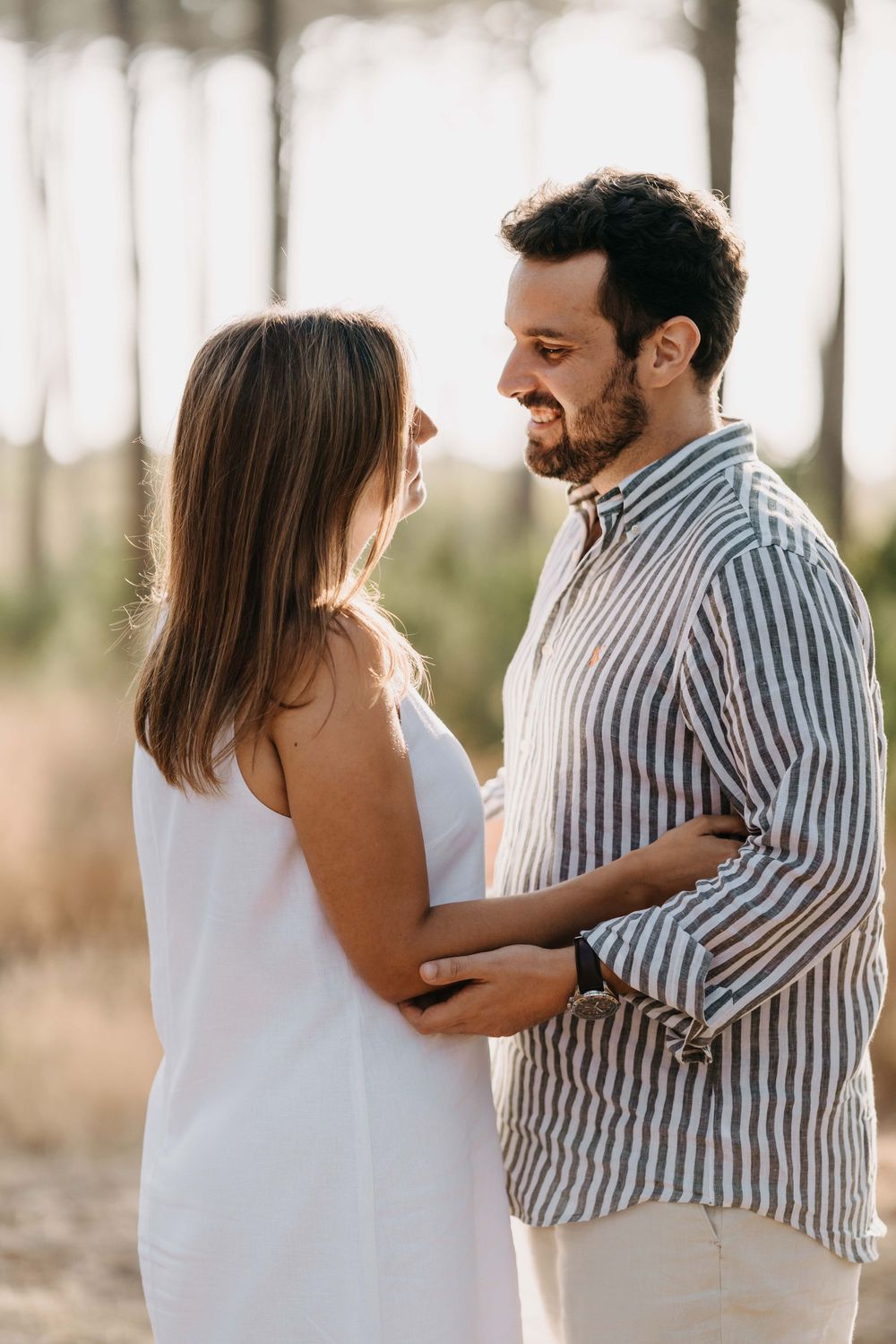 A couple in casual attire shares intimate moments together in a sunlit outdoor setting with trees in the background.