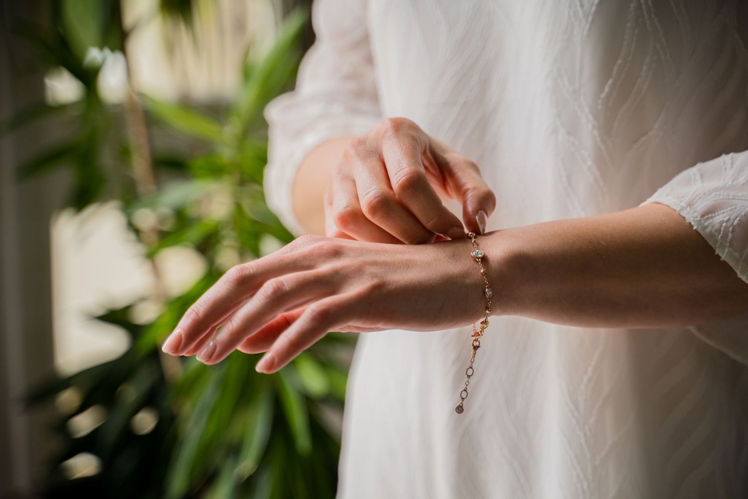 Delicate hands wearing a white dress sleeve fasten a dainty bracelet in soft natural lighting. Shot by Luminair Studio