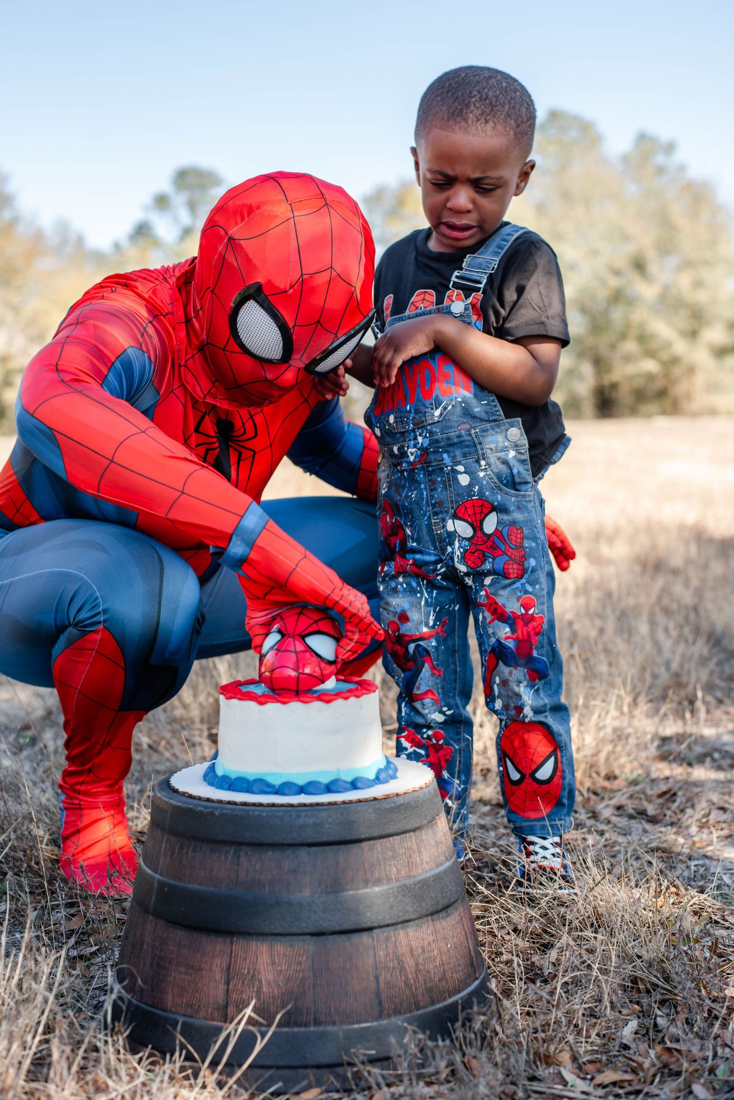 Spider-Man themed celebration with a decorated birthday cake placed on a rustic barrel outdoors.