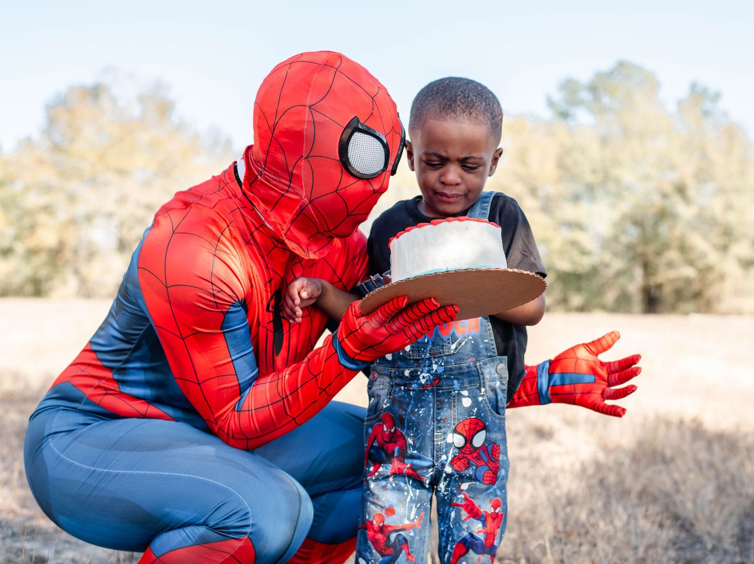 Spider-Man cosplayer crouches down and interacts playfully with a young fan at an outdoor event.