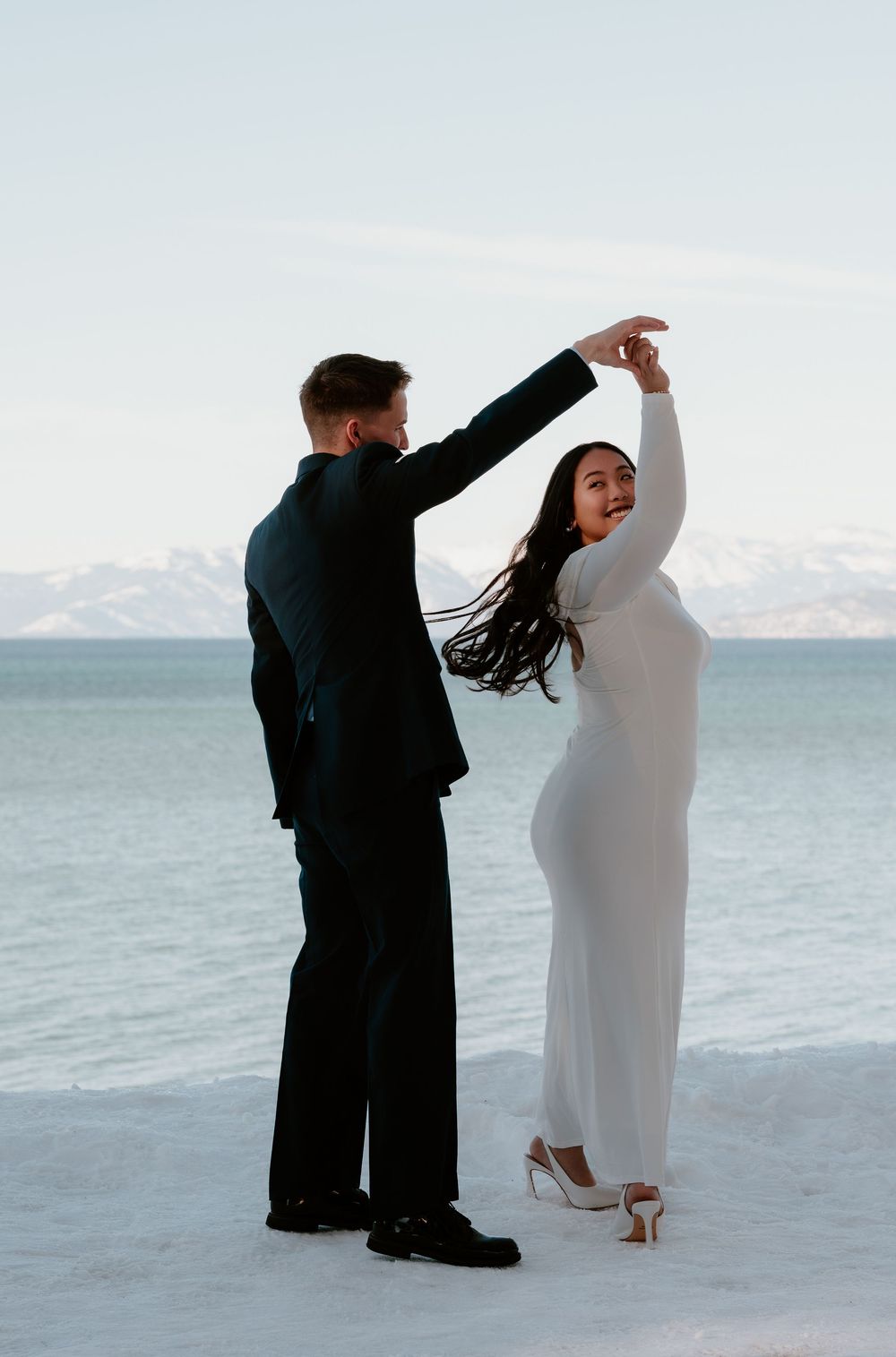 A couple dancing together on a snowy landscape with a serene lake and mountains in the background.