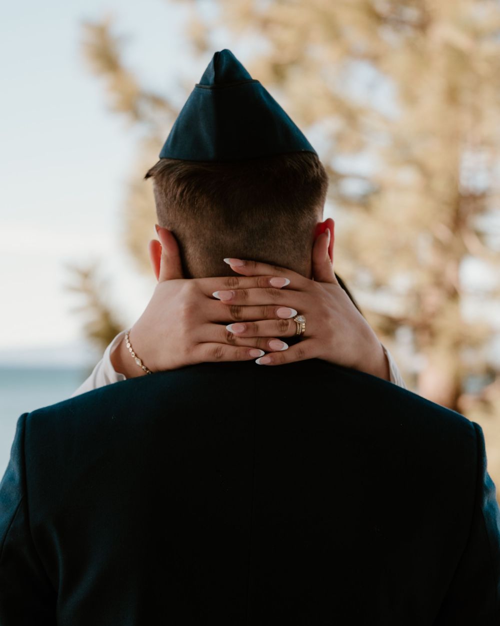 Back view of someone wearing a black yarmulke touching their head with both hands in a contemplative pose.