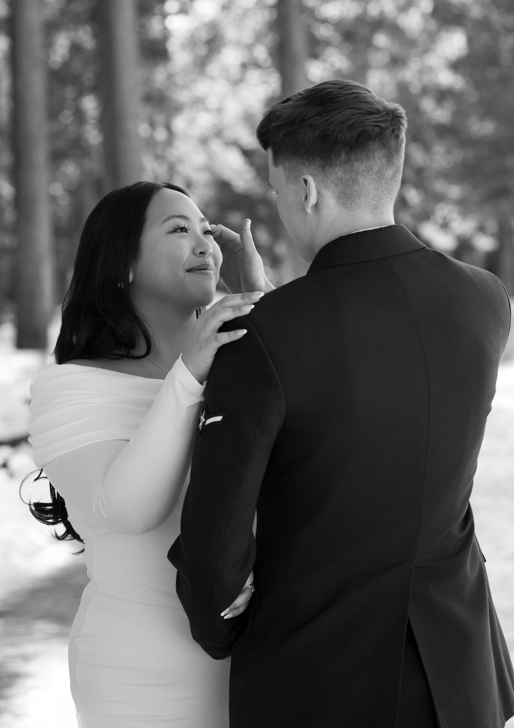 Black and white romantic wedding photo showing a tender moment between a couple in a white dress and black suit outdoors.