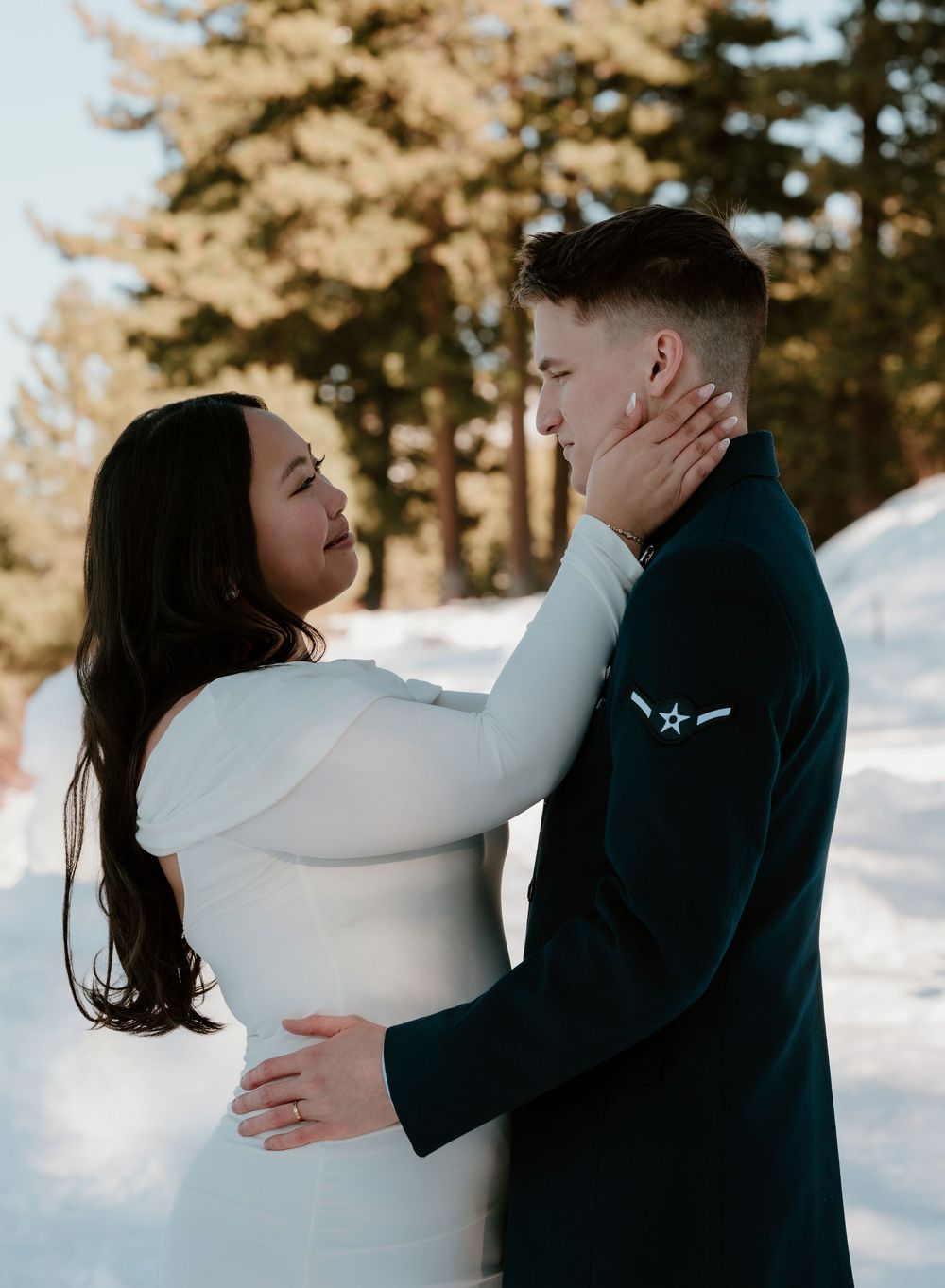 A romantic winter engagement photo showing a tender moment between a couple in formal wear against a snowy backdrop.