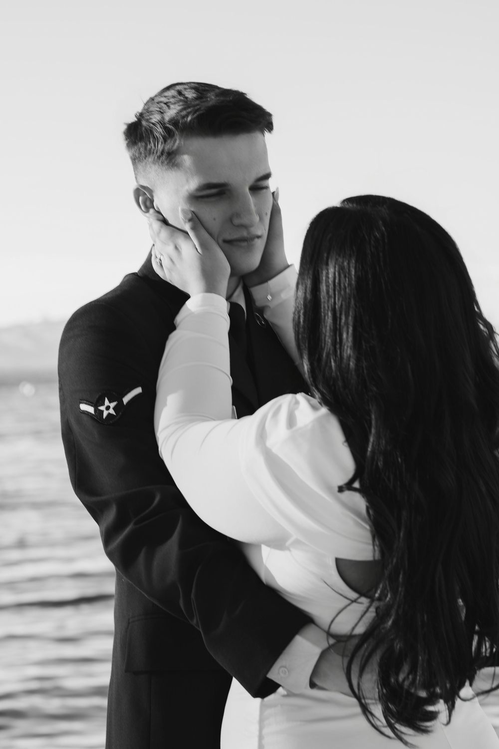 An intimate black and white moment between a couple in formal attire by the water.