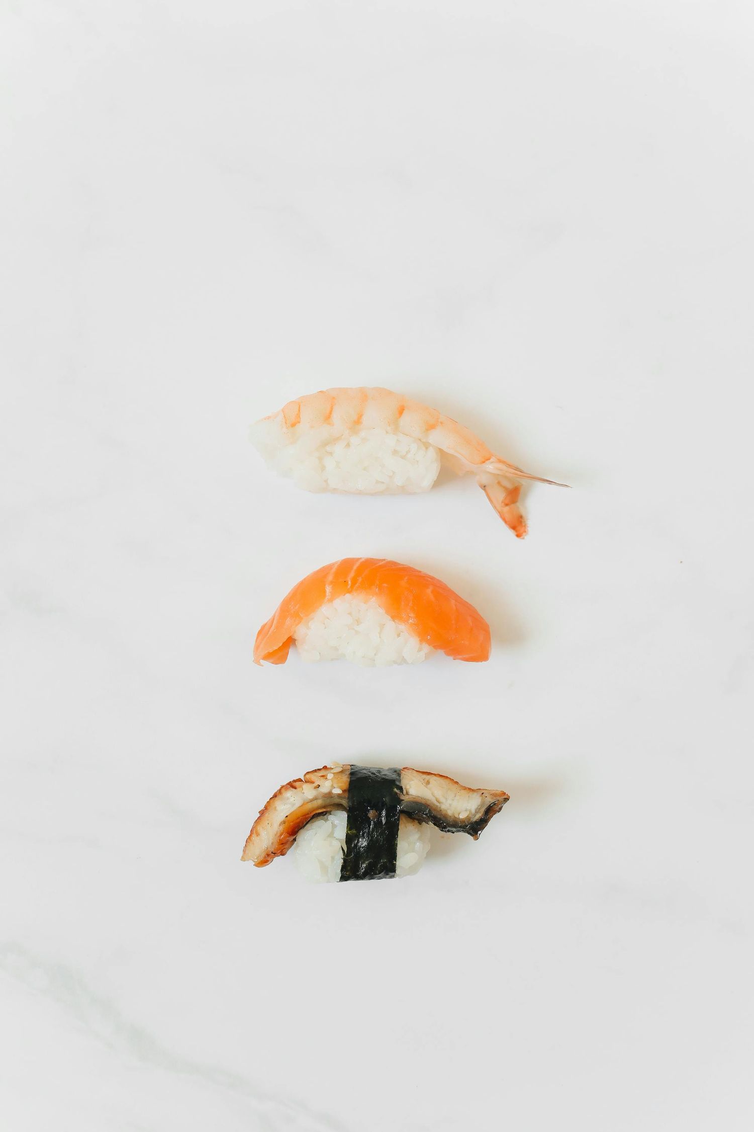 Close-up of fresh shrimp nigiri sushi with salmon and cucumber rolls on black slate plate with pickled ginger.