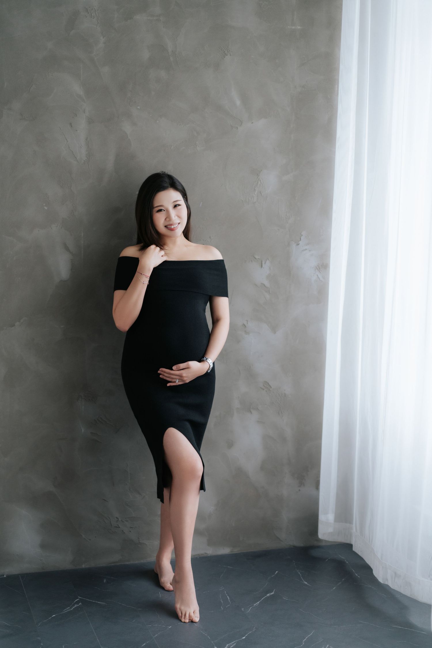Woman in black dress poses elegantly against concrete wall in minimalist portrait series.