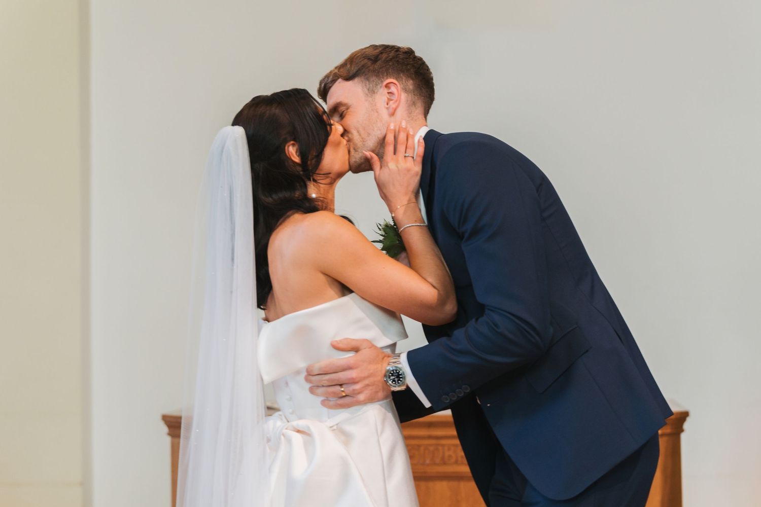A couple in formal wedding attire share their first kiss during their wedding ceremony.