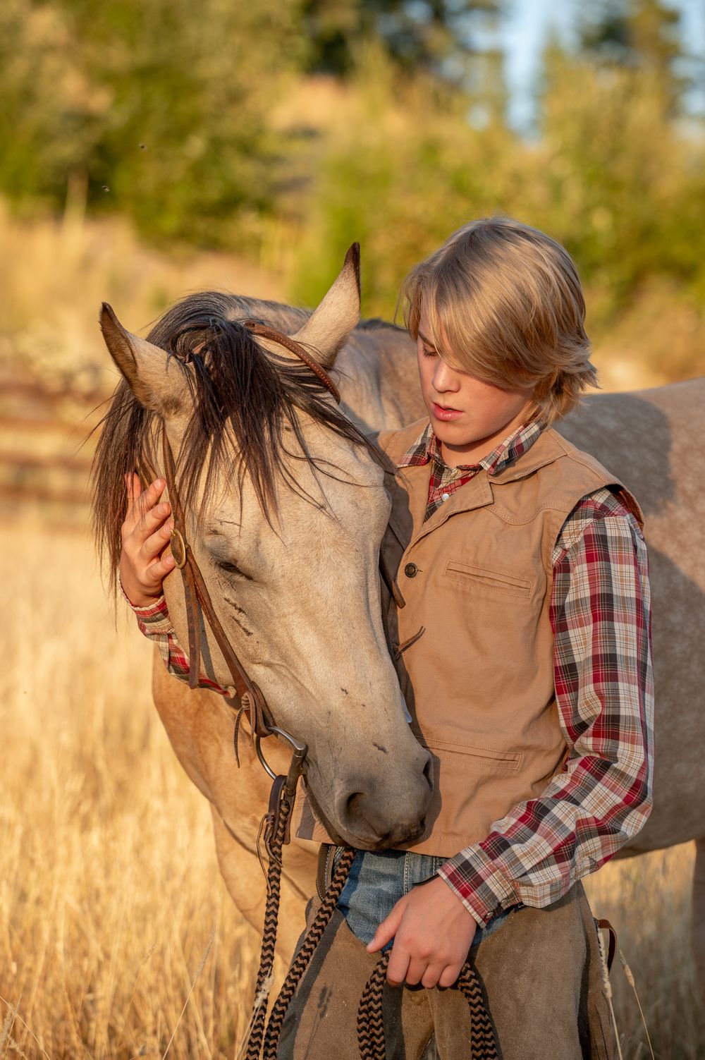 A tender moment between a horse and rider in a golden field at sunset wearing western ranch attire.
