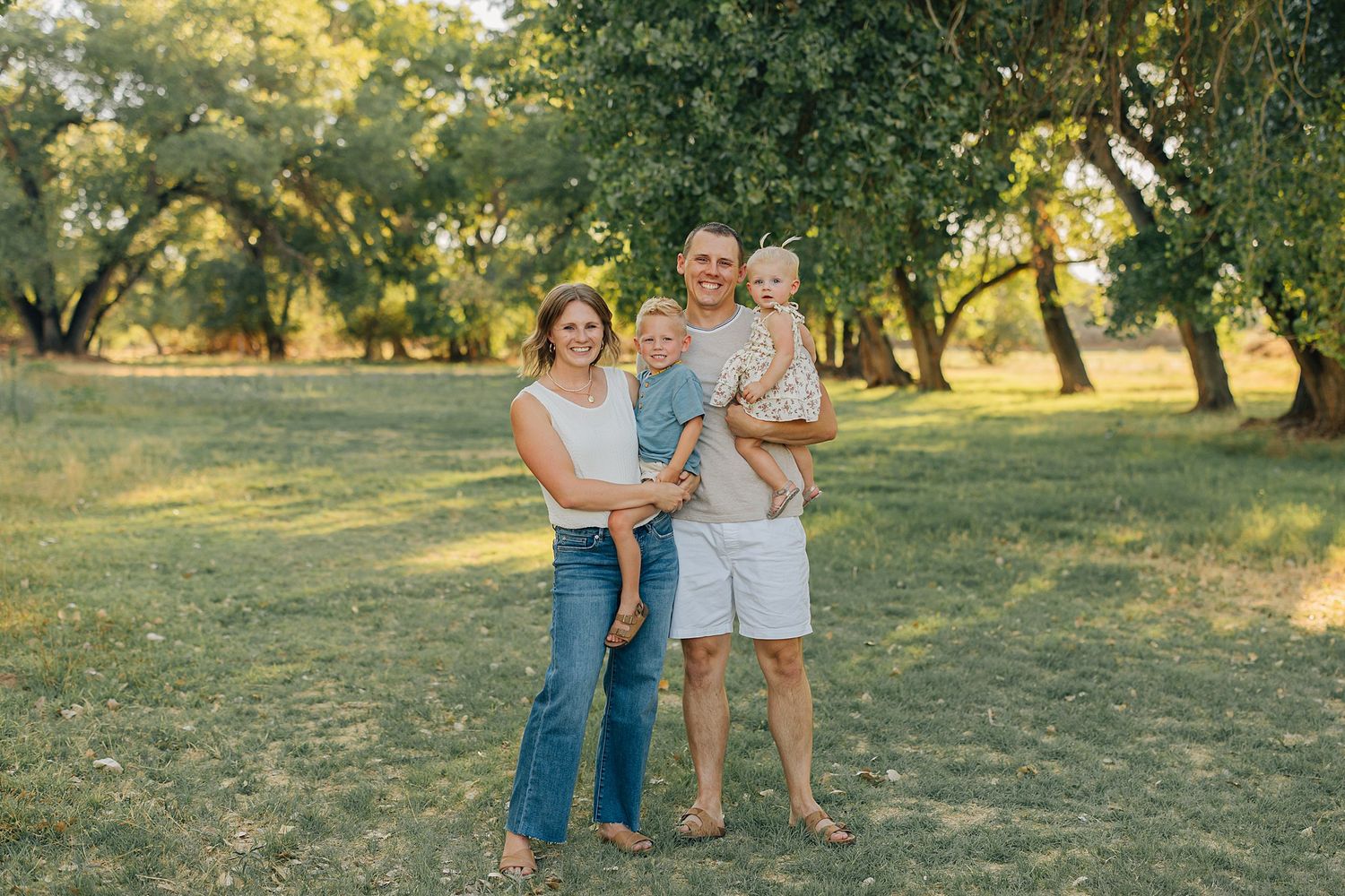 A group of people stand together in a grassy field during golden hour sunlight.