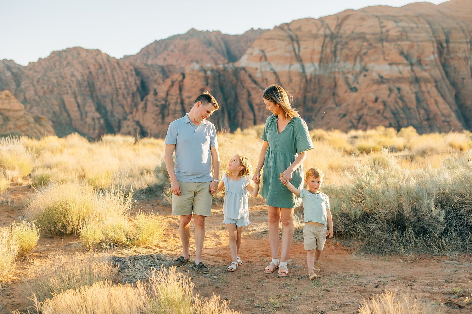 A group walks along a desert trail with red rock formations in the background during golden hour.