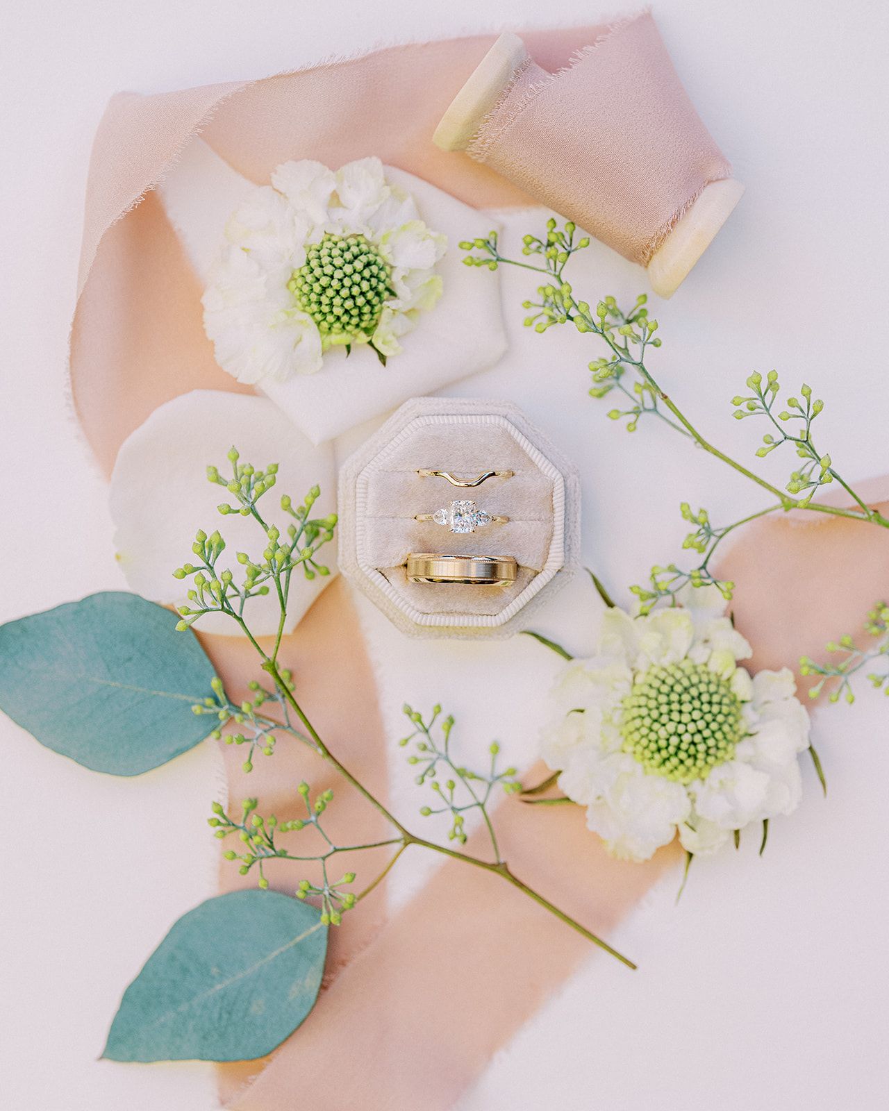 Wedding rings in clear hexagon box surrounded by white flowers and eucalyptus leaves.
