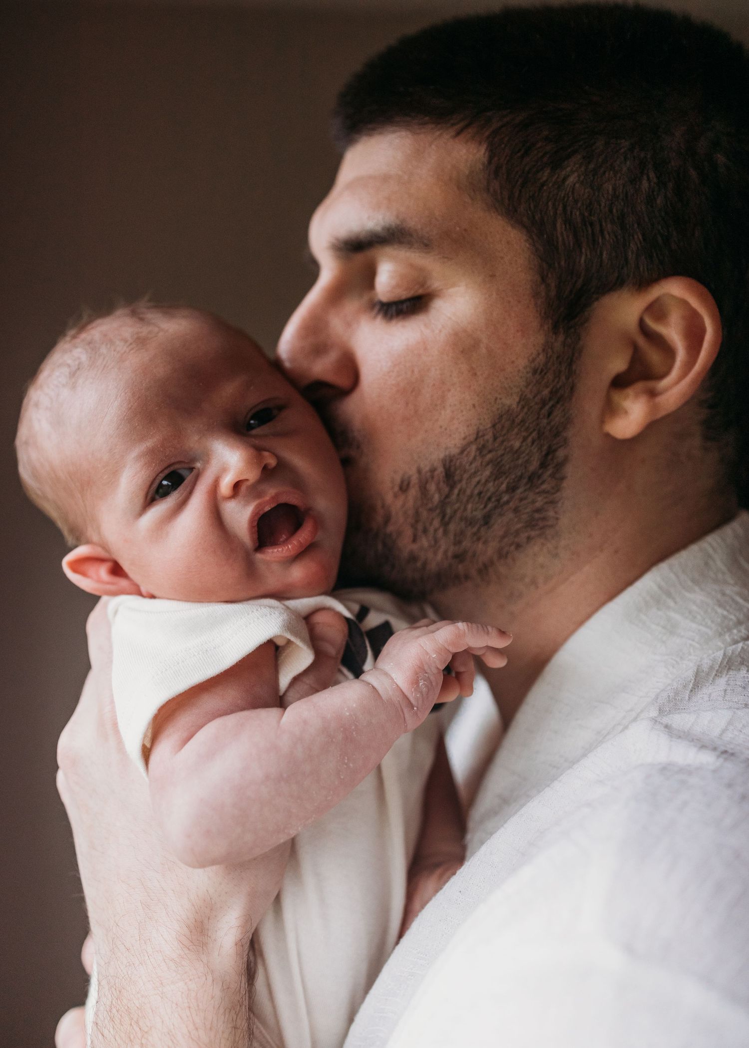 A tender moment between a parent and baby as they share an intimate kiss while the infant makes an expressive face.