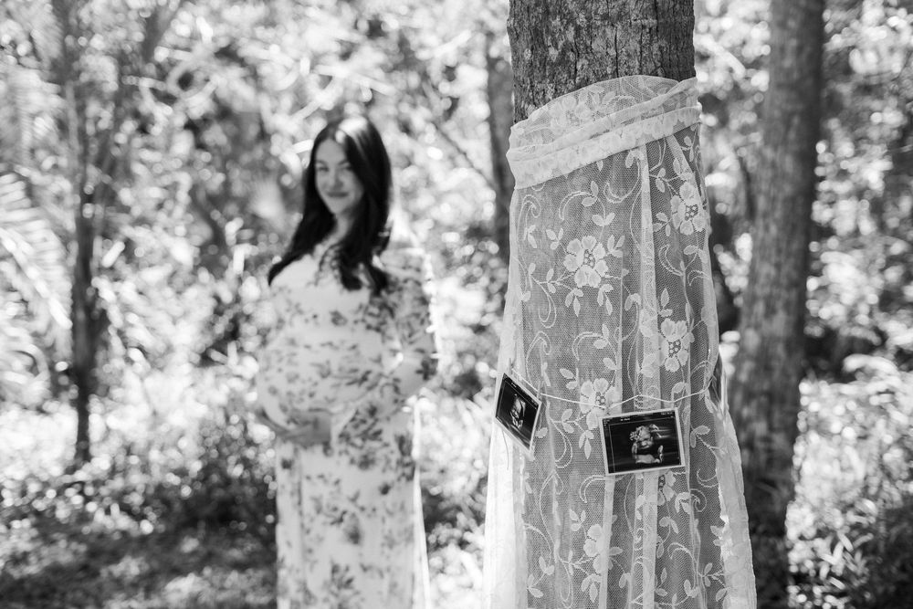 Black and white photograph of a person standing in a forest with light filtering through the trees.