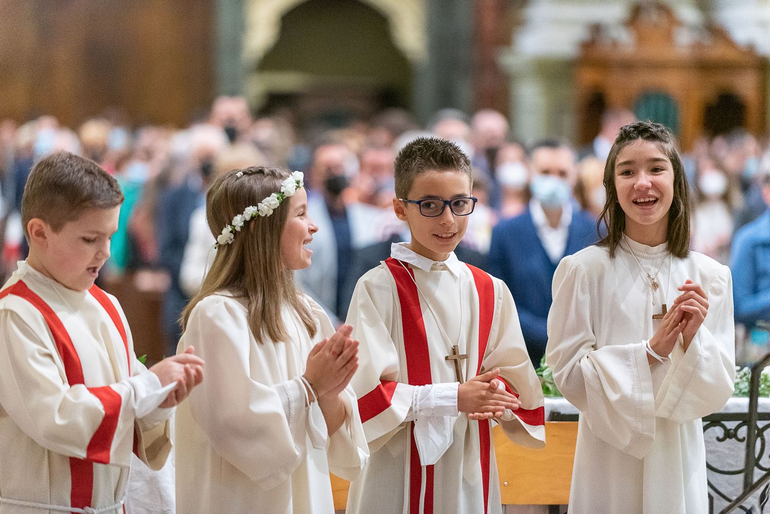 Altar servers in white robes and red sashes participating in a church ceremony.