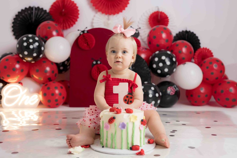 Festive first birthday party setup with red, black and white balloon decorations and a smash cake.