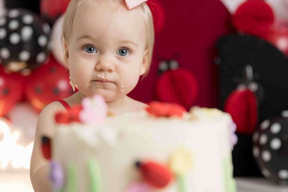 A baby sits in front of red and black polka dot decorations at a festive party setting.