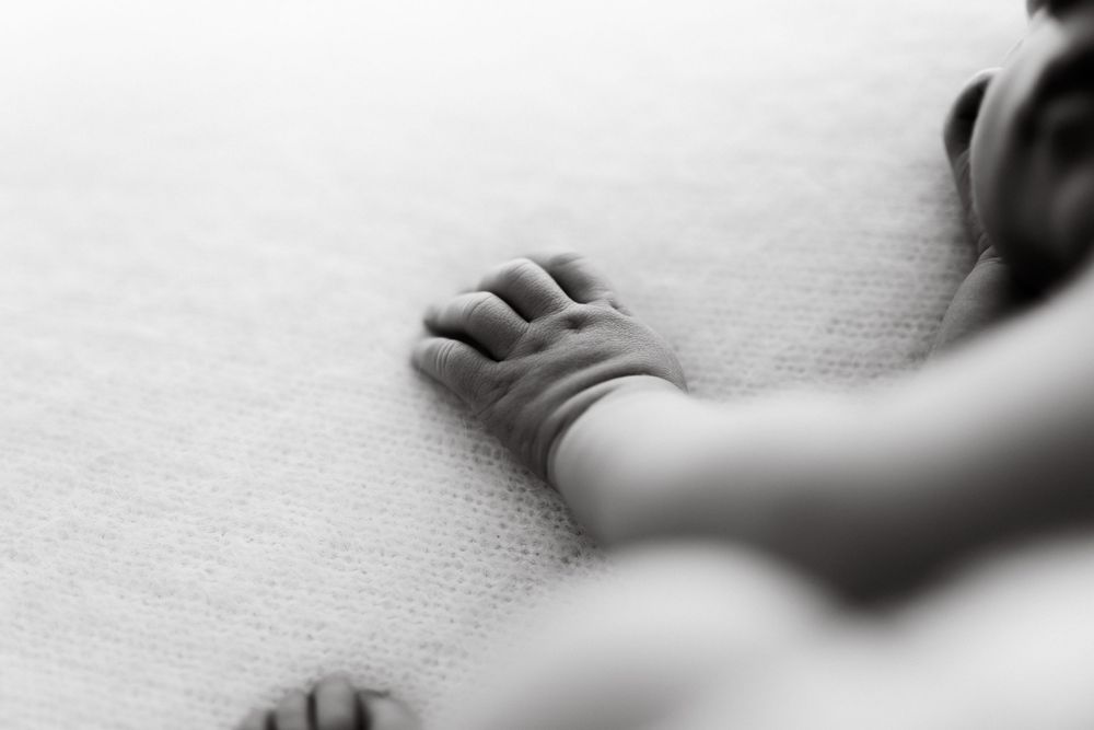 Gentle close-up of tiny baby feet wrapped in soft white blankets against light background.