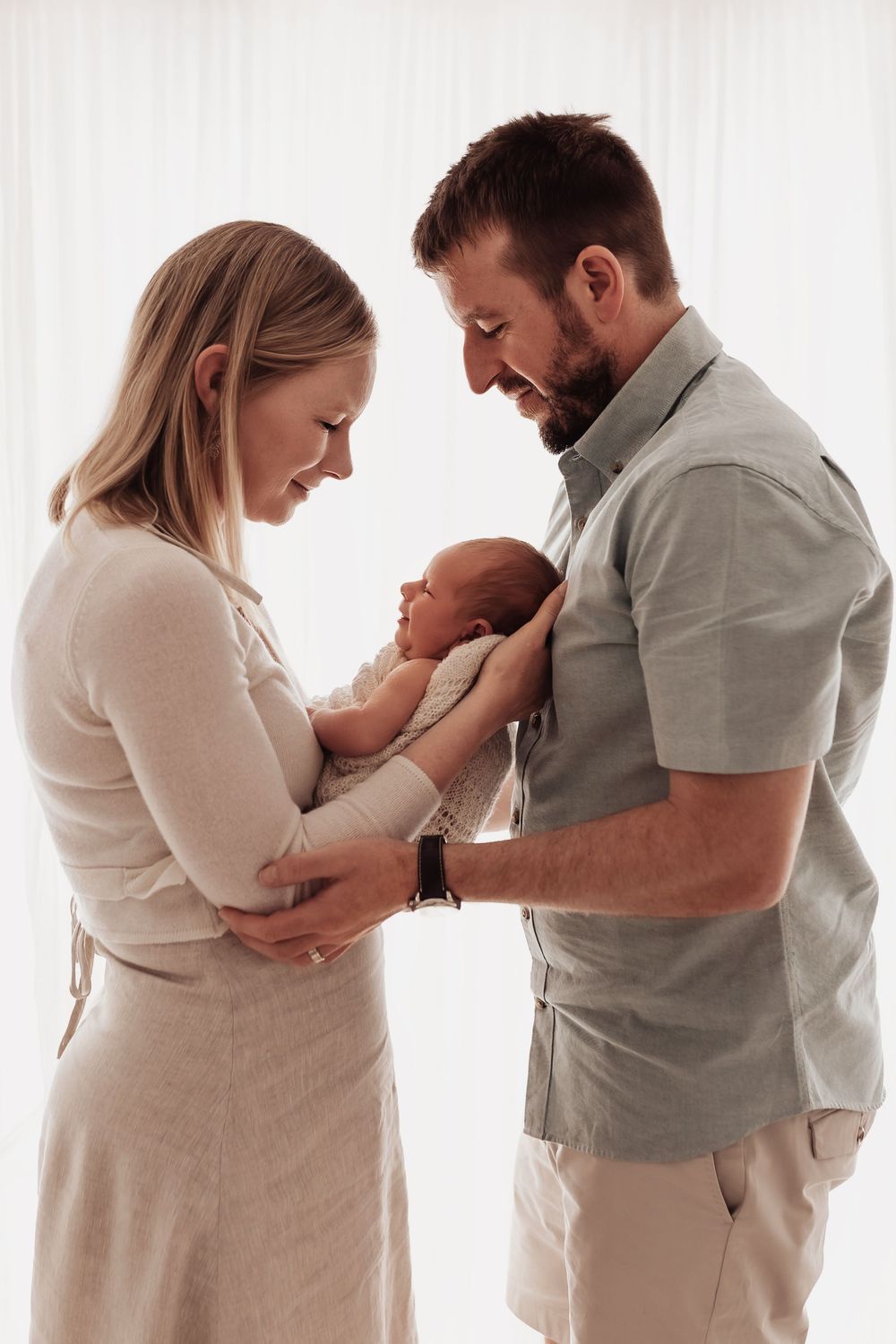 Family portrait sequence showing parents in white and grey clothing bonding with their newborn baby.