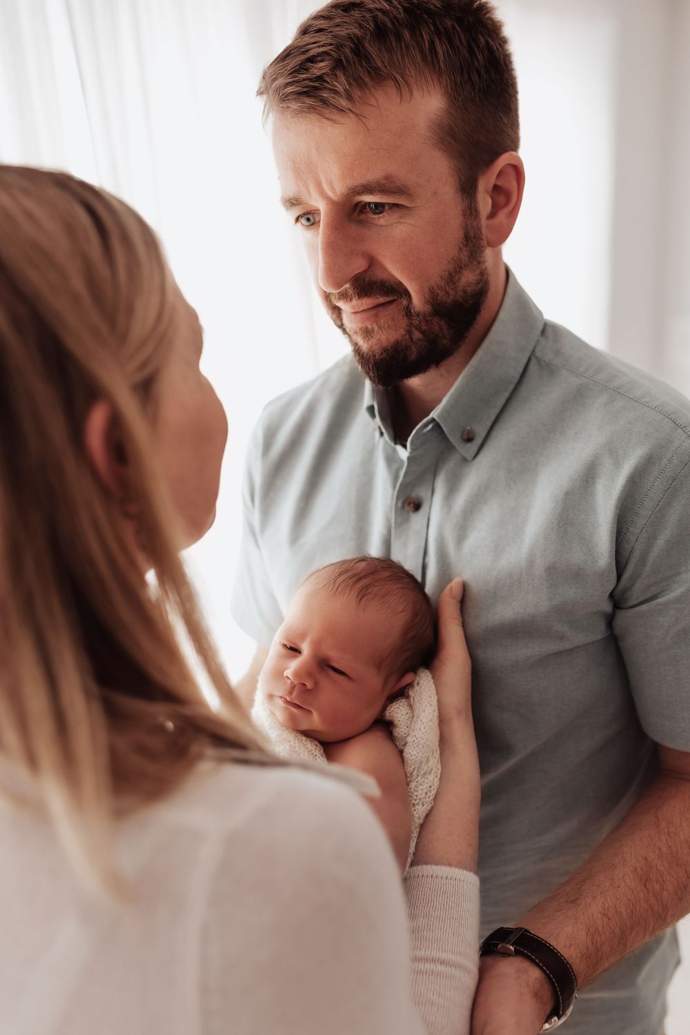 Parents share an intimate moment with their newborn baby in a bright, minimalist setting.