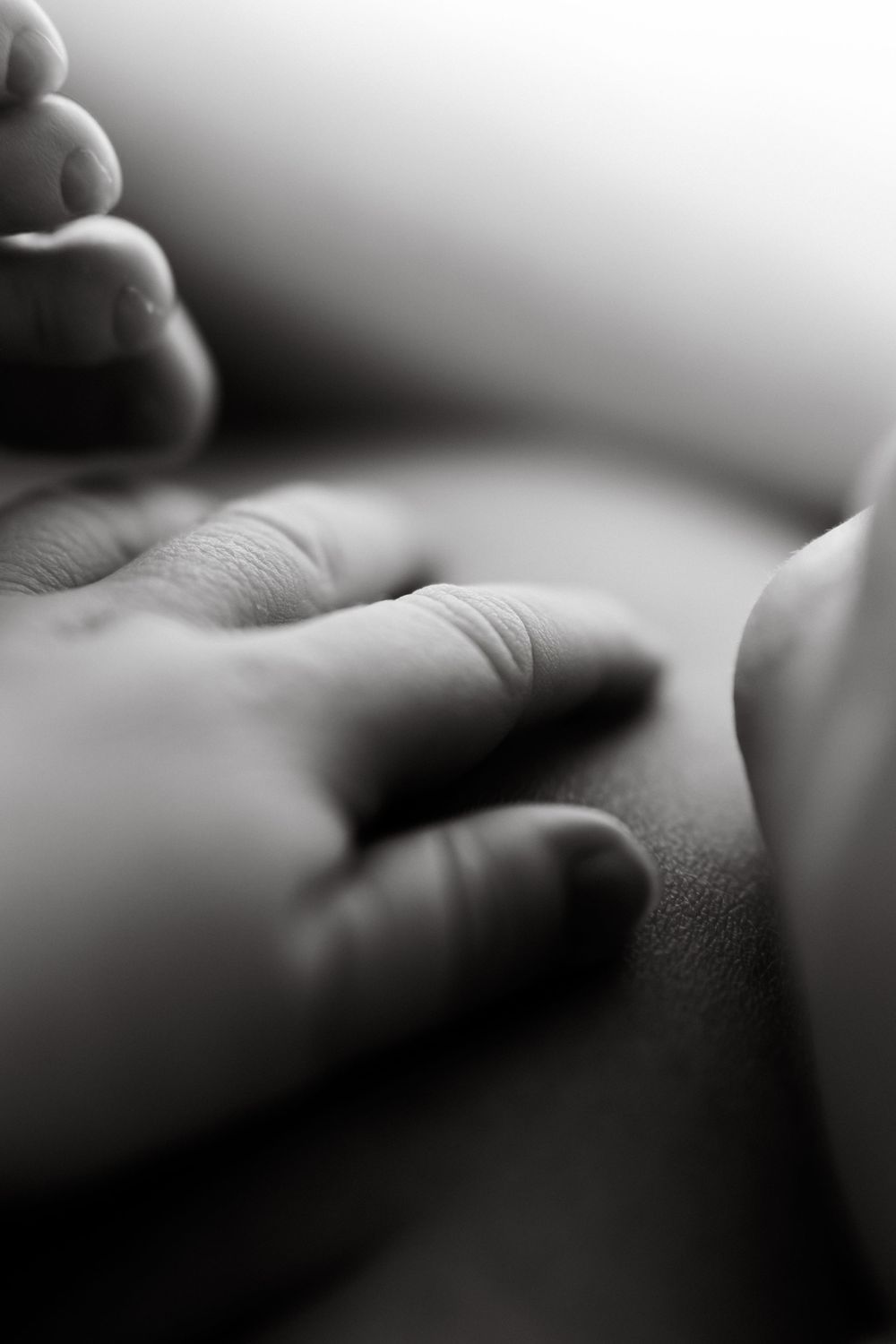 Close-up black and white image of gentle fingers touching skin in soft focus.