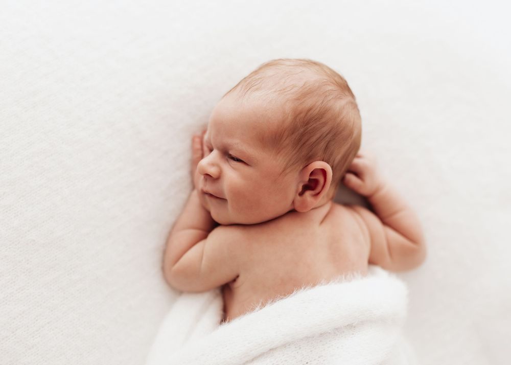 Peaceful newborn baby sleeping on soft white blanket in gentle natural lighting.