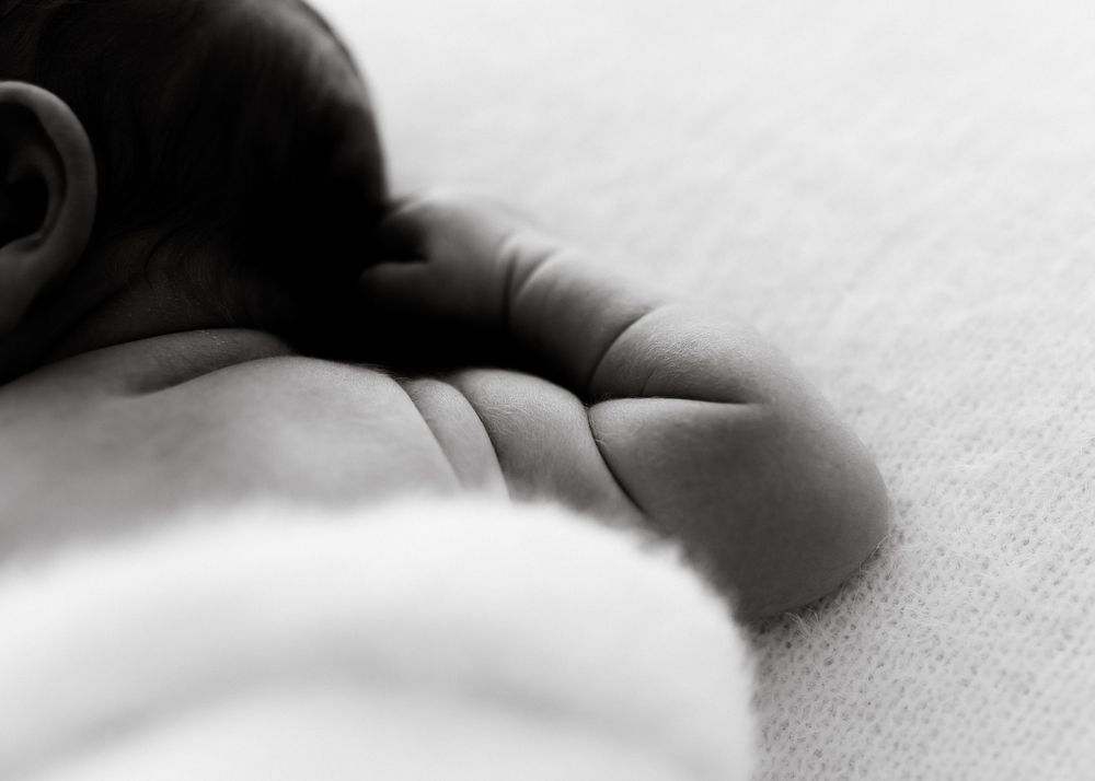 Black and white artistic close-up of sleeping infant wrapped in soft fabric.