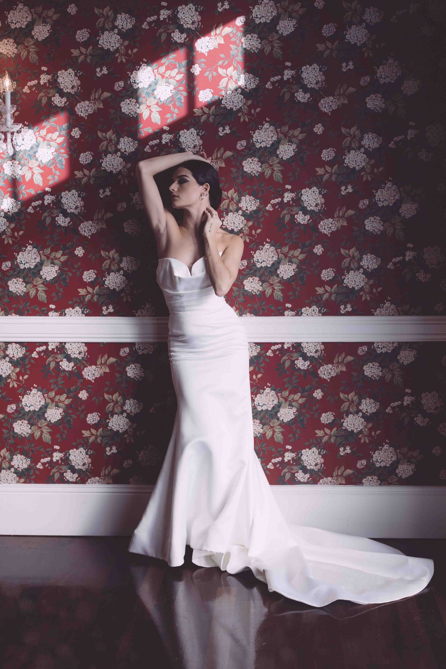 A figure in a white dress poses gracefully against a floral wallpapered wall in a series of artistic movements.