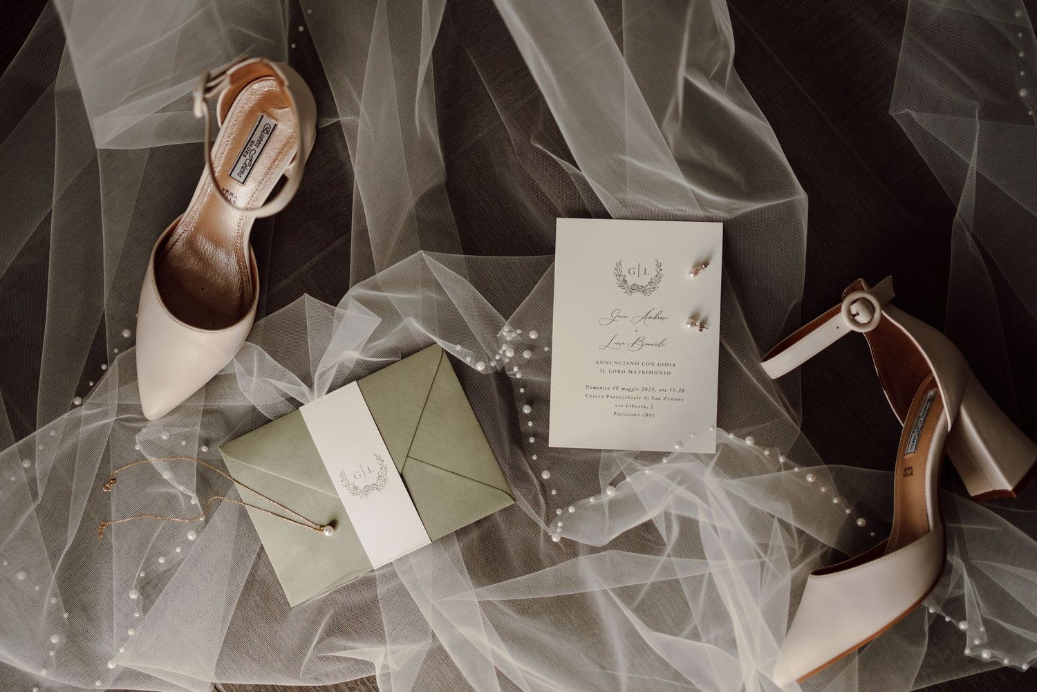 Bridal flat lay featuring ivory heels, wedding invitation, and pearl-adorned envelope on sheer tulle.