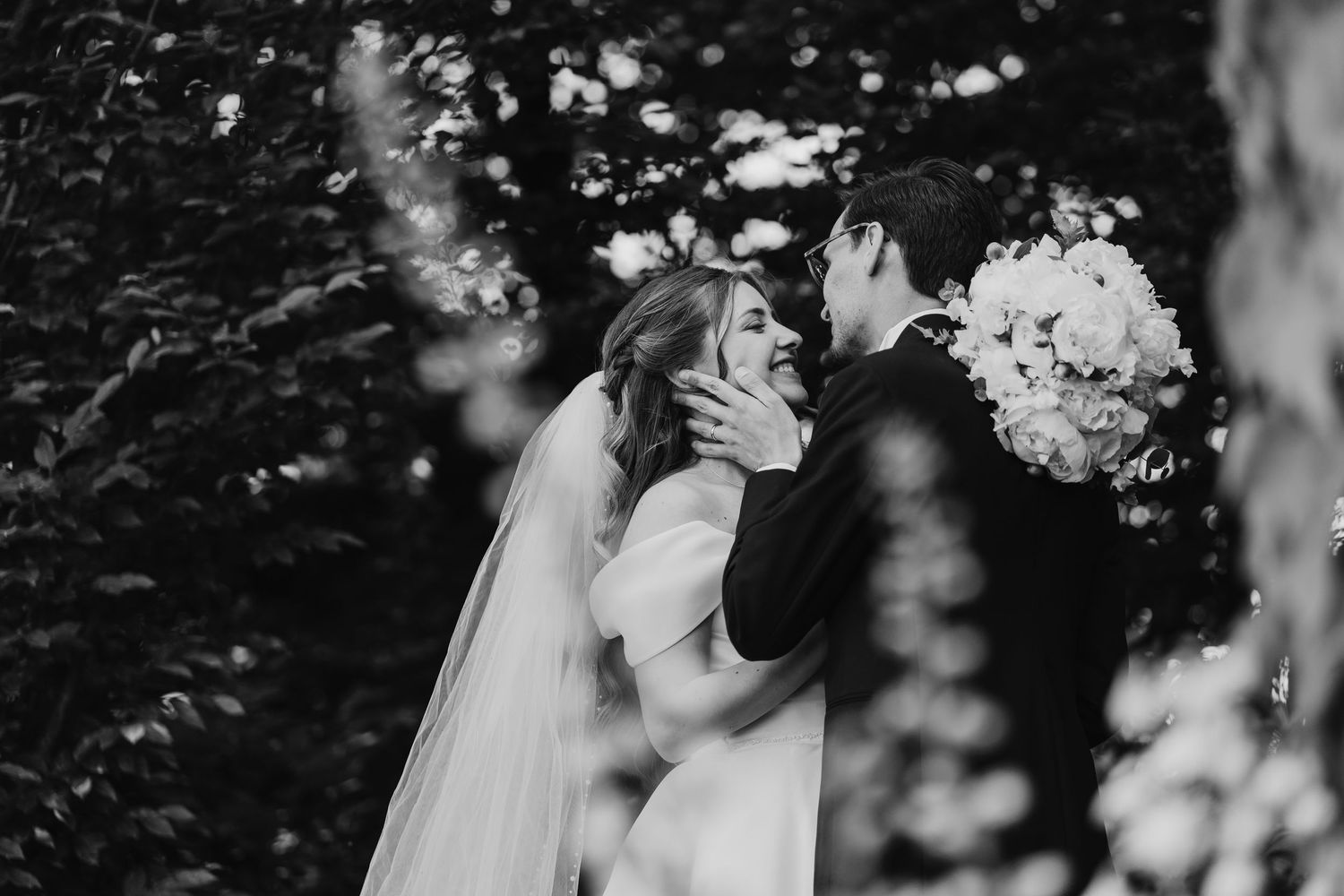 Black and white romantic portrait of bride and groom embracing in a garden.