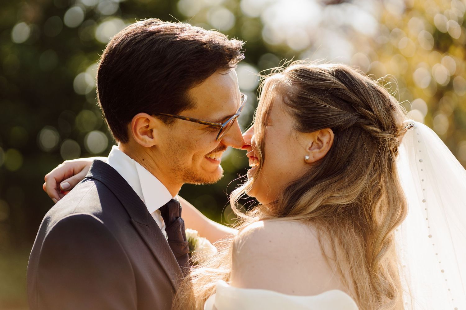 Bride and groom sharing an intimate moment, touching noses and smiling in warm golden sunlight.