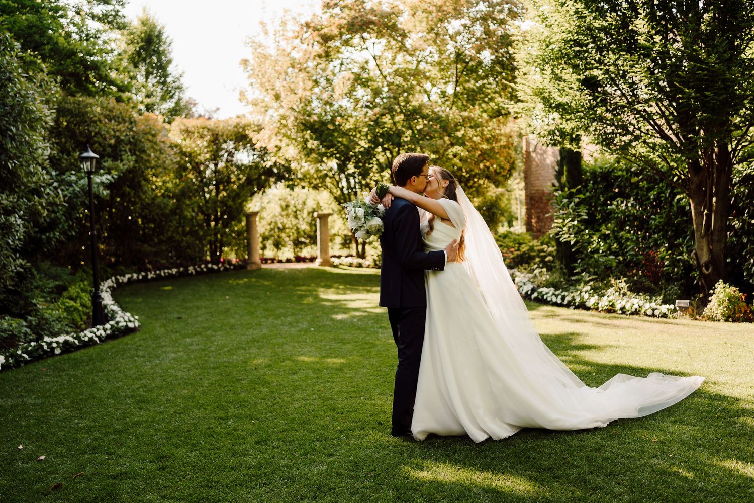 Bride and groom sharing a romantic kiss in a lush green garden on their wedding day.