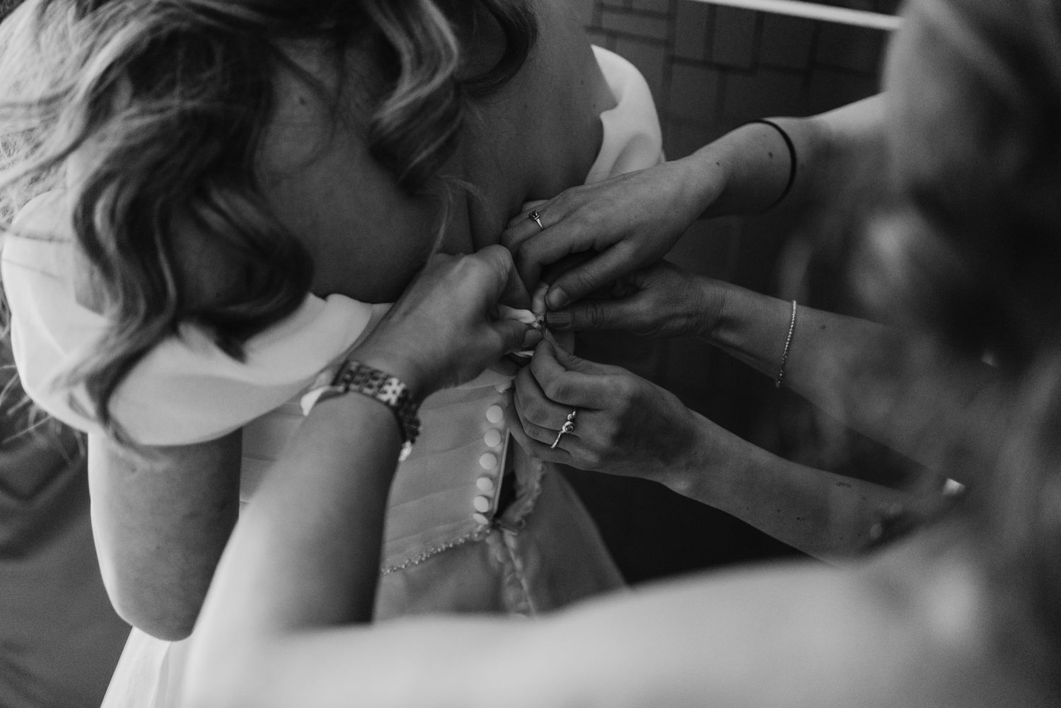 Black and white close-up of bridesmaids fastening the back of a bride's wedding dress.
