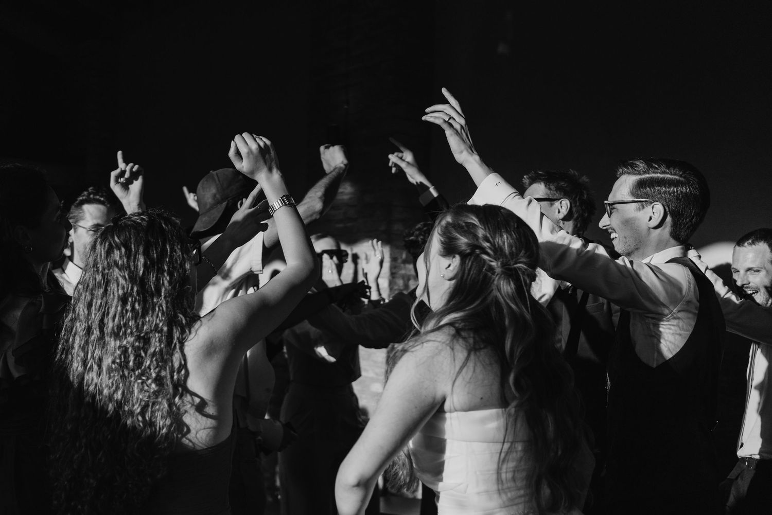 Energetic black and white photo of wedding guests dancing and raising hands at a lively reception party.