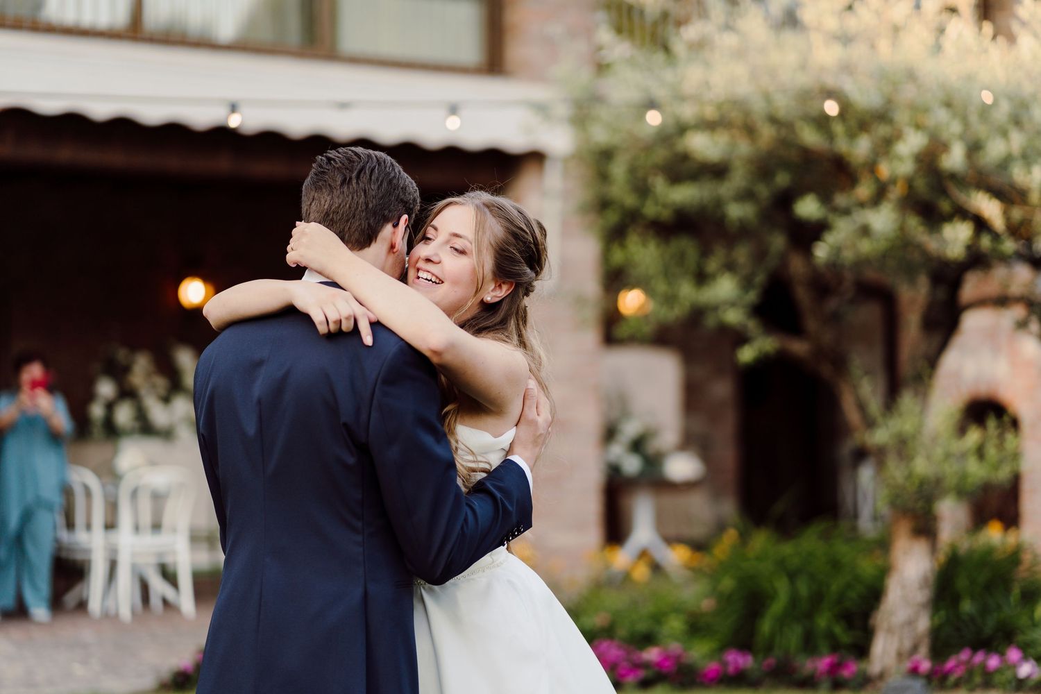Bride smiling joyfully while sharing first dance with groom in romantic outdoor garden reception venue.