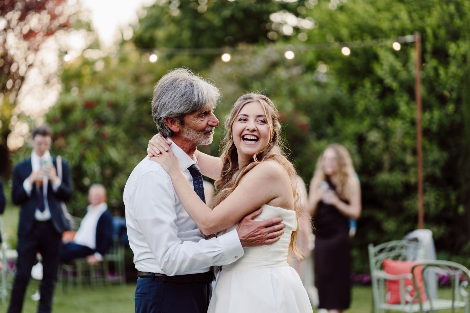Bride laughing with older gentleman during father-daughter dance at outdoor garden wedding reception.