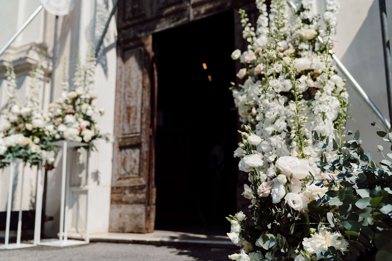 Elegant white floral arrangements framing the entrance of a church for a wedding ceremony.
