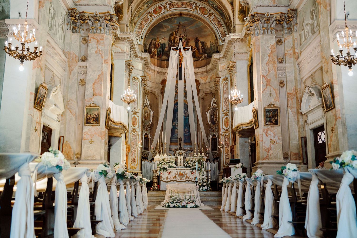 Ornate baroque church interior decorated with white ribbon pew bows for a wedding ceremony.