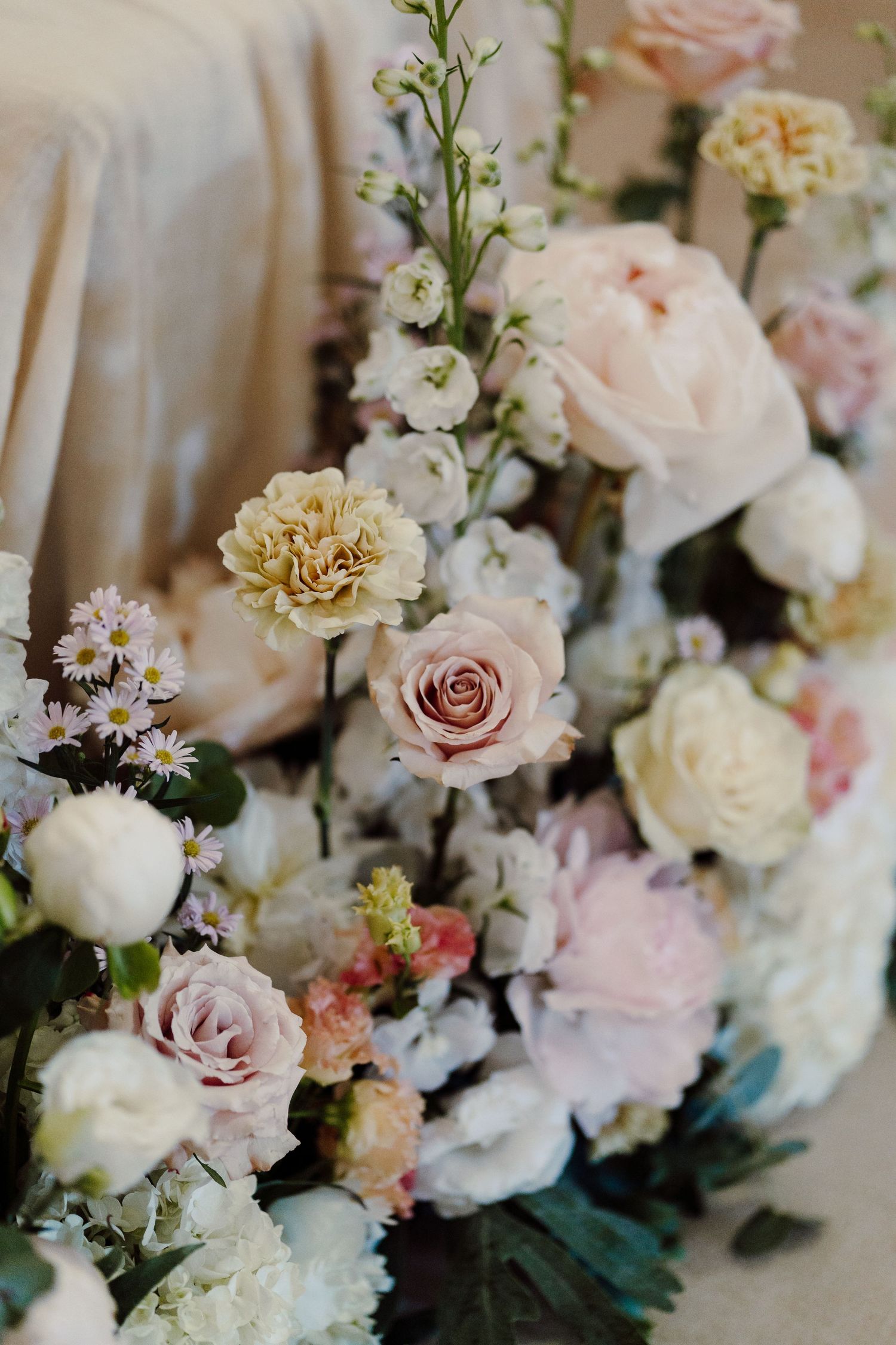 Lush arrangement of blush pink roses, carnations, and white flowers for a wedding decoration.