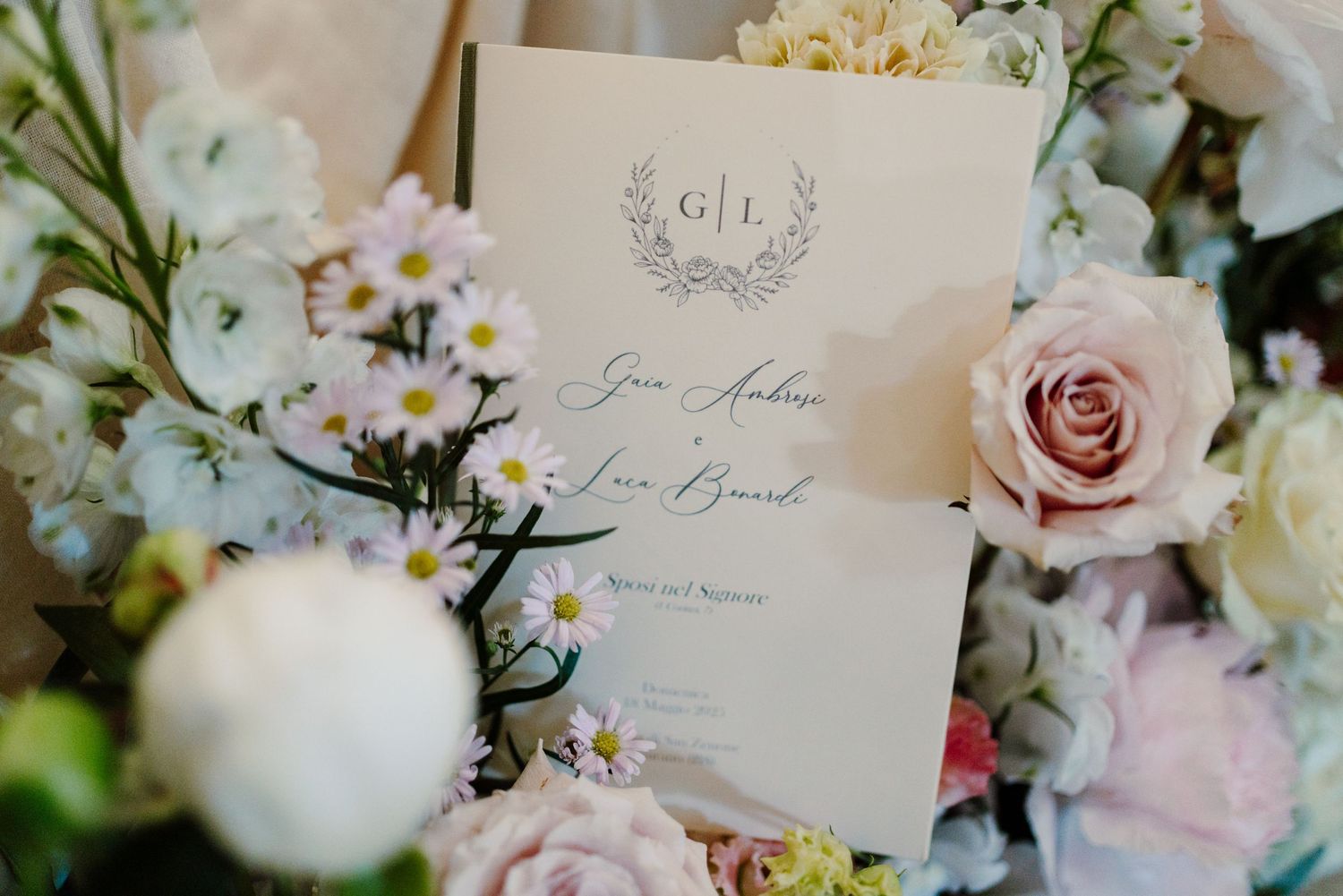 Wedding program card for Gia Andrea and Luca Beard surrounded by soft pastel flowers.